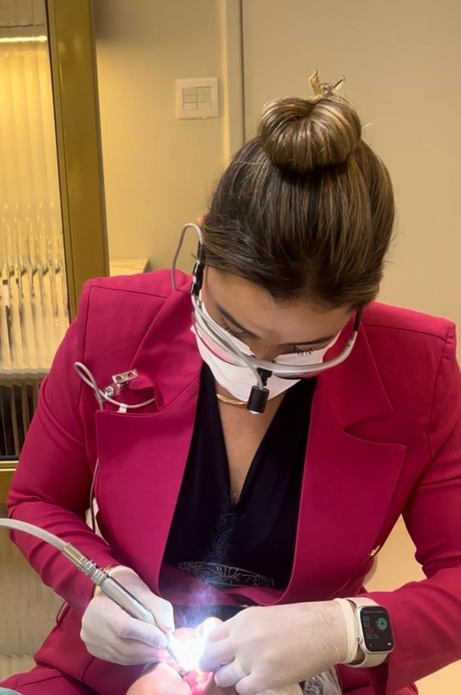 Dra. Lais Leal realizando procedimento estético com lupa de aumento e fotopolimerizador.